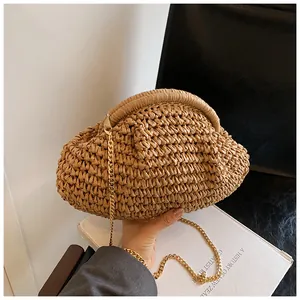 Détail du sac nuage en paille tressée kaki avec chaîne dorée tenu à la main par un mannequin