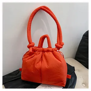Detail of bright orange quilted puffer bag with drawstring closure and dual handles
