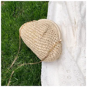 Détail d'un sac nuage tressé beige avec chaîne dorée sur fond d'herbe estivale