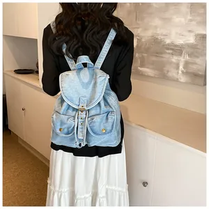Detalle de mochila de mezclilla azul claro con cierre de solapa y dos bolsillos frontales