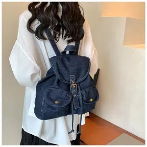 Detalle de mochila de mezclilla azul oscuro con cierre de cordón y botones de metal dorado