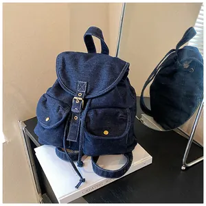 Detalle de una mochila de mezclilla azul oscuro con costuras blancas y hebillas doradas