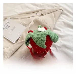 Close-up of handmade crochet strawberry bag with green leaf detail and white flower accent