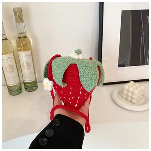 Close-up of handmade crochet strawberry bag with green leaf details and white flowers