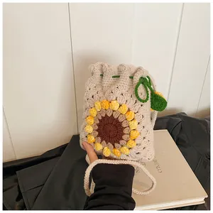 Detail of hand-knitted beige drawstring bucket bag with vibrant sunflower pattern and leaf decor