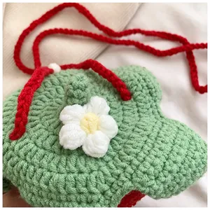 Close-up of handmade crochet strawberry bag with green texture and white flower detail