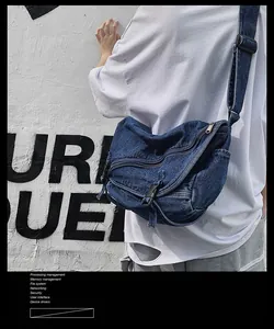 Dettaglio borsa a tracolla in denim blu con fibbia in plastica e tracolla larga su muro