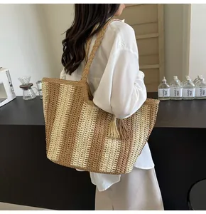 Dettaglio della borsa tote in paglia intrecciata con strisce verticali e nappa sulla spalla