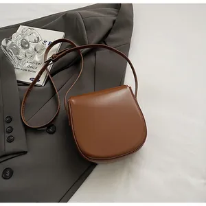 Braune Satteltasche aus Leder auf weißem Grund mit Blazer und ästhetischen Requisiten