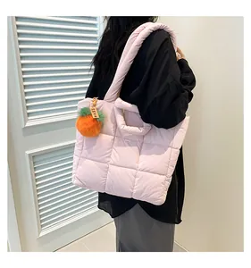 Close-up of pink quilted nylon tote bag with an orange pompom charm on a female model