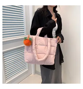 Detail of light pink quilted tote bag featuring a plush orange pom-pom charm accessory