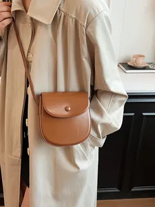 Braune Leder-Satteltasche für Damen, getragen mit einem schicken beigen Trenchcoat