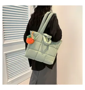Detail of light green quilted nylon tote bag with orange pompom and wooden charm