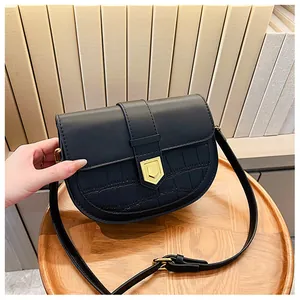 Detail of black saddle bag featuring faux crocodile texture and gold shield buckle