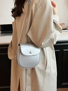 Silberne Satteltasche aus Kunstleder mit Metallic-Finish, getragen zum beigen Trenchcoat
