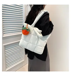 Detail of white quilted puffer tote bag with cute orange plush charm and wide shoulder strap