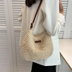 Dettaglio della borsa tote in paglia intrecciata con tracolla in pelle marrone e logo