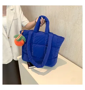 Detail of dark blue quilted puffer tote bag featuring a cute orange persimmon plush charm