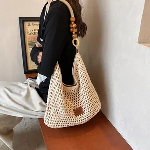 Detail of hollow knit beach bag featuring wooden bead shoulder strap and leather logo