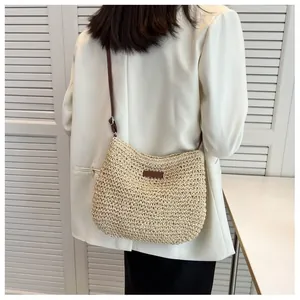 Dettaglio di una borsa a tracolla in paglia intrecciata beige con toppa e cinturino in pelle