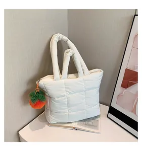 Detailed close-up of white quilted puffer tote bag with decorative plush charm on table