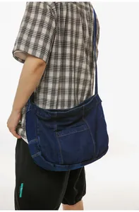 Detail of dark blue denim crossbody bag featuring contrast stitching and wide shoulder strap