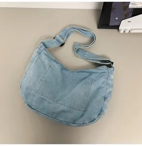 Macro detail of a light blue denim hobo bag with adjustable wide strap and front pockets