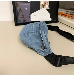 Detailed view of light blue denim waist bag with silver zippers on a minimalist desk