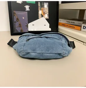 Detailed view of washed blue denim fanny pack with black zippers on a minimalist desk