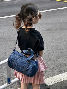 Detail of blue denim cylindrical kids bag with yellow stitching and metal hardware