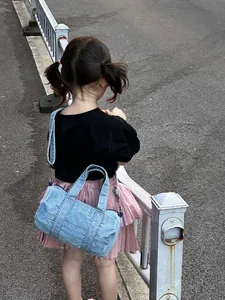 Toddler in outdoor street setting wearing a light blue denim cylinder crossbody bag
