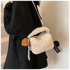Nahaufnahme der cremeweißen Plüschtasche mit Teddybär-Anhänger und gewebter Quaste