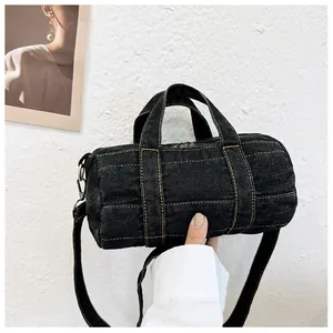 Detail of a mini navy denim cylinder bag featuring contrast yellow stitching and top handles