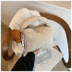 Detail der cremefarbenen Plüschtasche mit süßem Bärenanhänger auf Holzstuhl