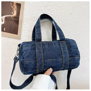 Detail of dark blue denim barrel bag with yellow contrast stitching and hand grip detail