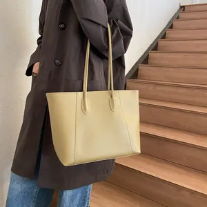 Side view of a beige matte leather tote bag with vertical stitching on model shoulder
