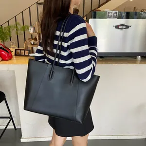 Lifestyle shot of a large black matte leather tote bag worn over the shoulder in a cafe