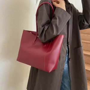 Lifestyle shot of a large red matte leather tote bag styled with a brown trench coat