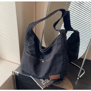 Detail of vintage black denim tote bag with brown stitching and brand leather patch