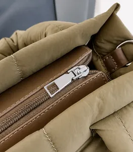 Detail of silver metal zipper puller on olive green quilted crossbody bag with brown trim