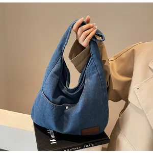 Detail of blue denim tote bag with leather logo patch and silver snap button closure