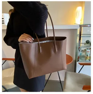 Brown faux leather tote bag with long straps worn by a model in a cozy cafe setting