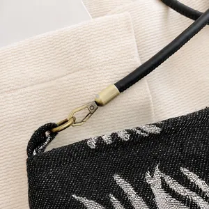 Detailed macro view of the antique bronze metal hook and black leather strap on embroidered bag