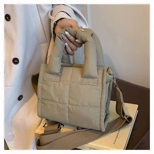 Detail of beige quilted shoulder bag with soft handles and wide brown woven strap