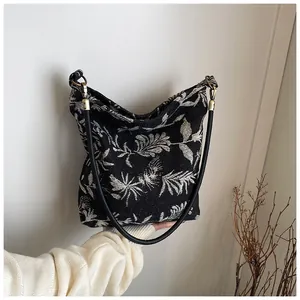 Detail of hand-held canvas tote bag featuring white leaf pattern and brass hardware