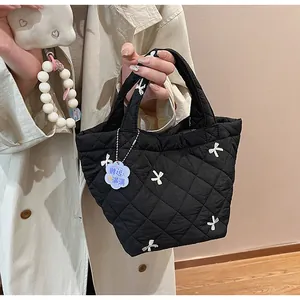 Detail of black quilted tote bag with bow embroidery and beaded charm accessory