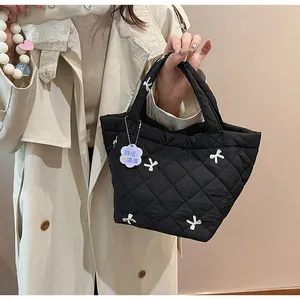 Close-up of black quilted handbag with white bow and flower charm held by model