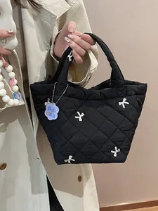 Quilted black handbag with white bow embroidery and floral charm held by a model