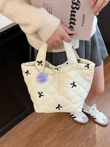 Cream quilted tote bag with black bow embroidery and purple flower charm pendant