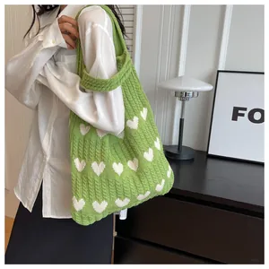 Detail der grünen Strick-Tote-Bag mit weißem Herzmuster getragen von Model in weißem Hemd